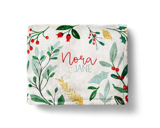 Personalized holiday blanket featuring watercolor mistletoe, holly, and berries with custom baby name in red and light blue on a soft white minky fabric.