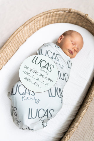 Blue baby boy swaddle set with matching name reveal sign, ideal for coming-home outfits.