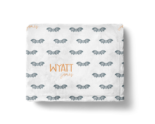Personalized Halloween bat baby blanket with custom name in orange text on soft white minky fabric, featuring cute gray bat pattern – cozy spooky season throw for babies, toddlers, and kids.