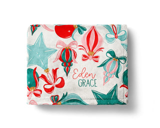 Personalized Christmas baby blanket with red, green, and teal ornaments, bows, and stars, featuring custom name in festive font.