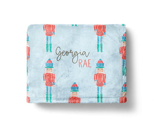 Personalized Christmas baby blanket with nutcracker soldier design on a light blue background, featuring the name “Georgia Rae” in festive script.