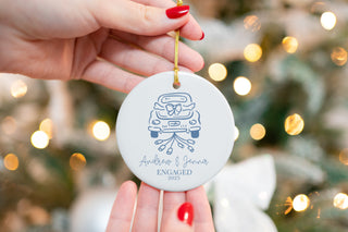 Custom ceramic ornament featuring a vintage car with a bow and trailing cans, personalized with couple’s names “Andrew & Jenna” and year 2025 — engagement keepsake.