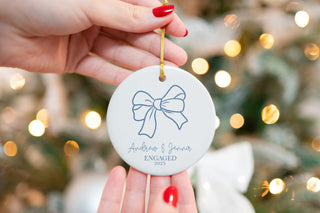 Custom ceramic ornament featuring a simple blue bow design, personalized with couple’s names “Andrew & Jenna” and year 2025 — elegant engagement keepsake.