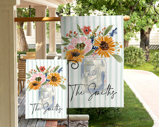 Personalized fall yard flag displaying watercolor floral bouquet in a mason jar with elegant script family name on a vintage striped background.