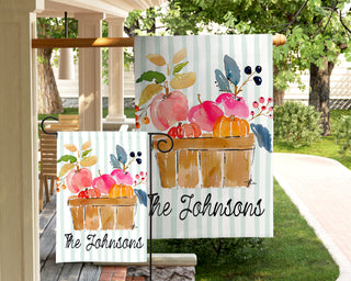Personalized fall yard flag displaying a watercolor harvest crate filled with apples and pumpkins on a soft green striped background.