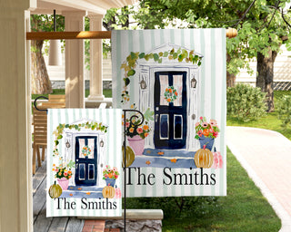 Personalized autumn garden flag featuring a navy front door, seasonal wreath, pumpkins, and colorful flowers with a custom last name.