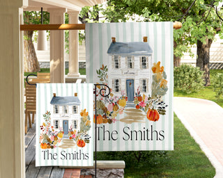 Personalized autumn garden flag featuring a navy front door, seasonal wreath, pumpkins, and colorful flowers with a custom last name.