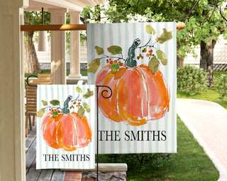 Personalized autumn garden flag displaying a hand-painted watercolor pumpkin with seasonal greenery and a custom last name.