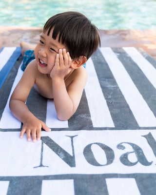 Children wrapped in custom embroidered beach towels – fun summer swim accessories in pink, green, and gray stripes.