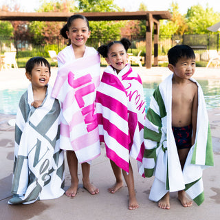 Four happy kids wrapped in personalized striped beach towels by the pool – custom summer swim accessories for children