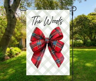 Personalized Christmas garden flag with red plaid bow and family name displayed outdoors – The Navy Knot holiday decor