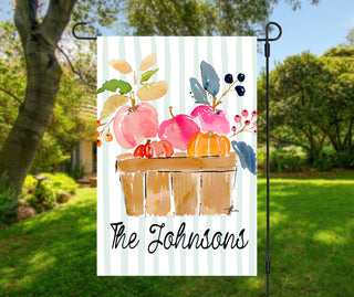 Personalized fall garden flag featuring watercolor apples, pumpkins, and a rustic wooden crate with a custom family name on a sage striped background.