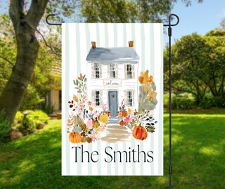 Personalized fall garden flag featuring a watercolor navy front door with a floral wreath, pumpkins, flower pots, and a custom family name on a sage striped background.