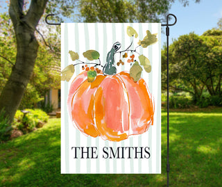 Personalized pumpkin garden flag featuring a large watercolor orange pumpkin with fall leaves and a custom family name on a soft sage striped background.