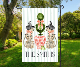 Personalized Halloween garden flag featuring two Staffordshire-style dogs wearing witch hats beside a topiary in a chinoiserie planter with a custom family name.