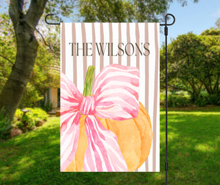 Personalized topiary garden flag featuring a boxwood topiary with a peach bow in a chinoiserie planter and a custom family name on a blush striped background.