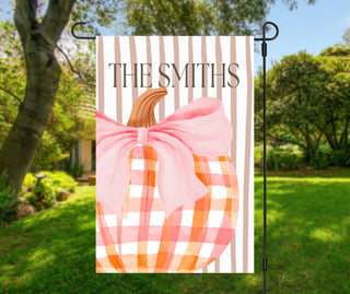 Personalized topiary garden flag featuring a boxwood topiary with a peach bow in a chinoiserie planter and a custom family name on a blush striped background.