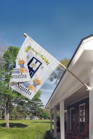 Custom fall garden flag with a watercolor front door, autumn pumpkins, floral planters, and personalized family name for farmhouse porch decor.