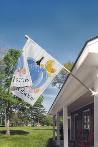 Personalized autumn garden flag displaying a hand-painted watercolor pumpkin with seasonal greenery and a custom last name.