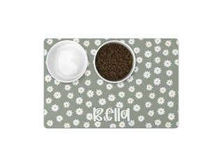 Personalized sage green pet food mat with white daisy floral pattern, featuring custom name in playful font, placed under dog food and water bowls